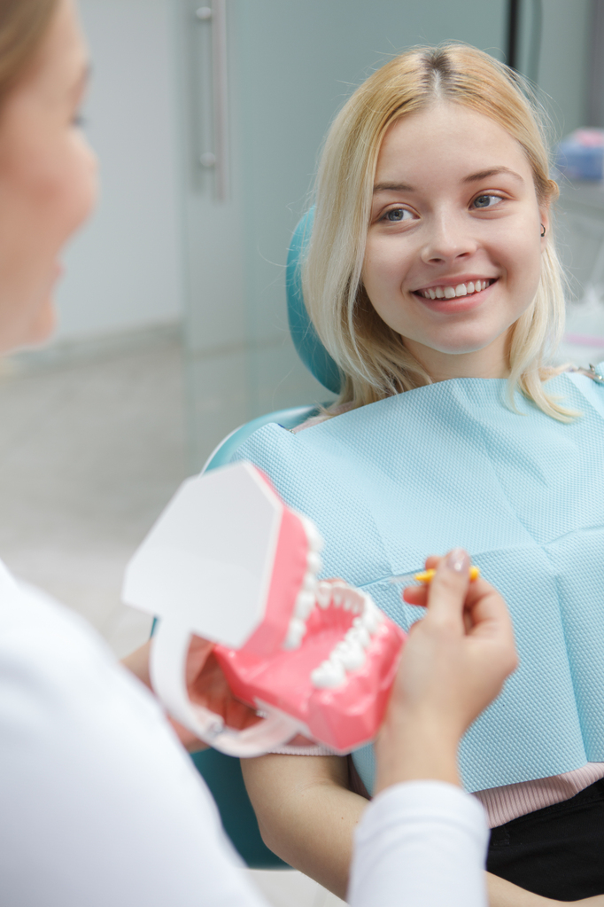 vertical-shot-cheerful-young-woman-smiling-her-dentist-sitting-dental-chair.jpg