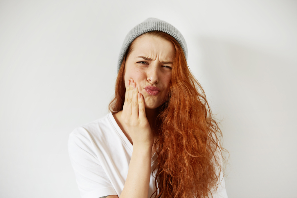 headshot-redhead-teenage-woman-pressing-her-cheek-with-painful-expression.jpg