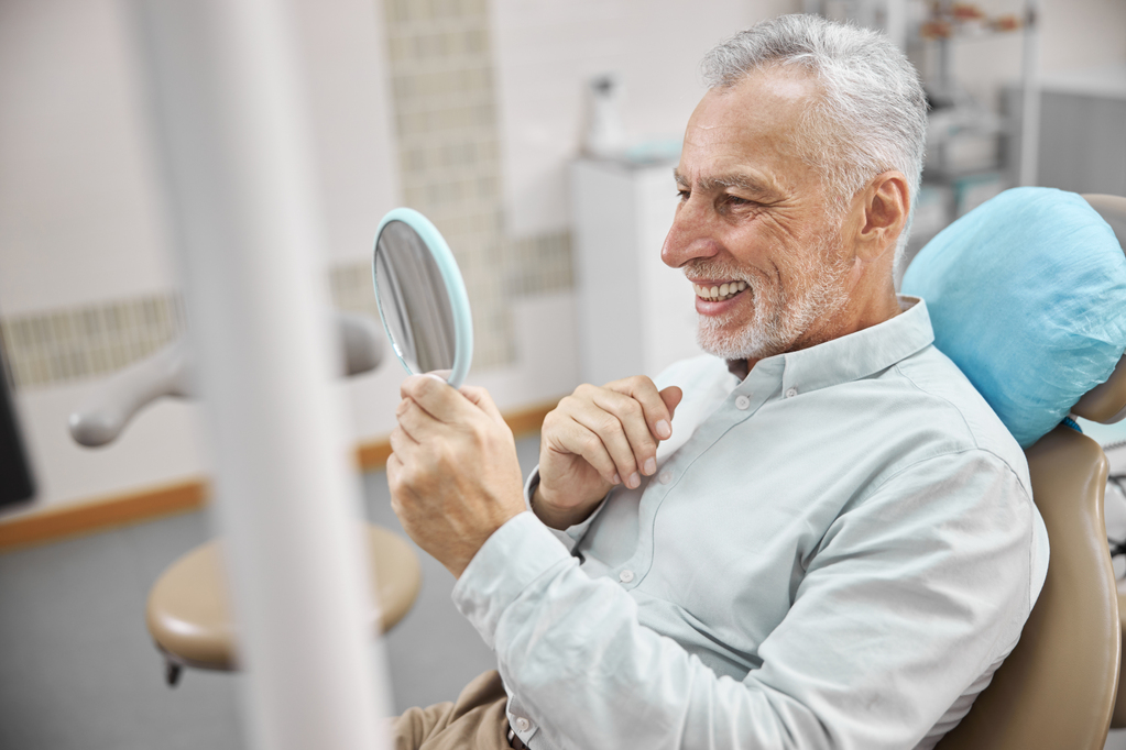 contented-elderly-man-sitting-dental-chair-checking-out-his-new-teeth-while-looking-mirror.jpg